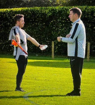 Two people chatting on the pitch, one holding a linesman's flag and a water bottle