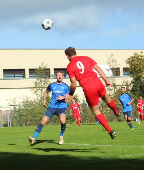 A St Brelade FC player going for a diving header